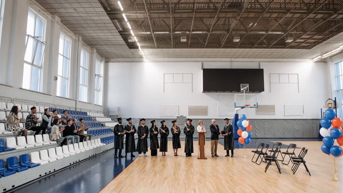 A graduation ceremony held in an indoor gymnasium with graduates and an audience.