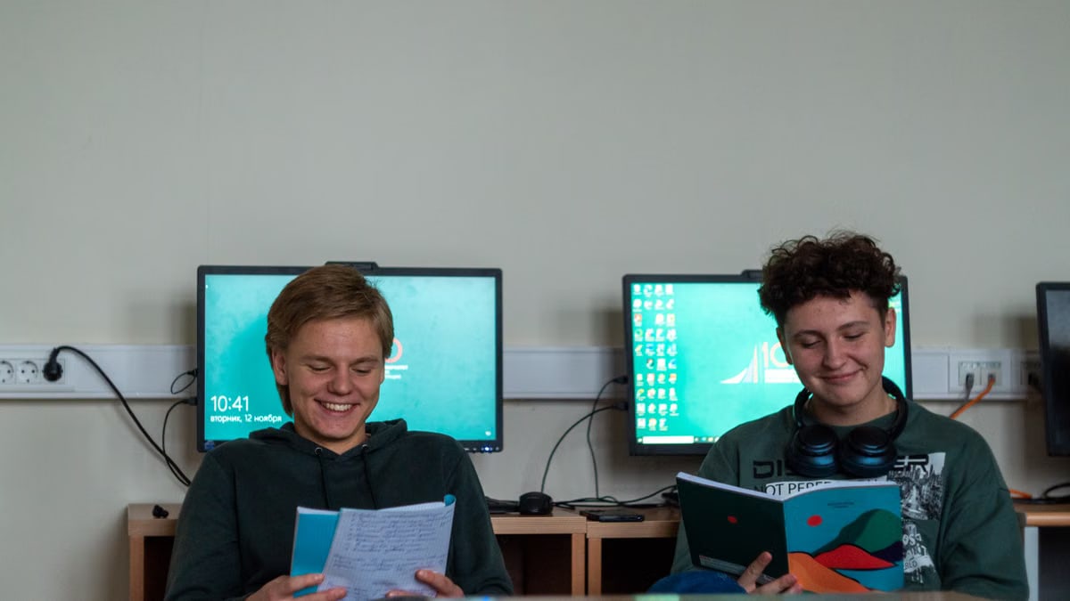 Two young adults reading booklets in an indoor computer lab setting.